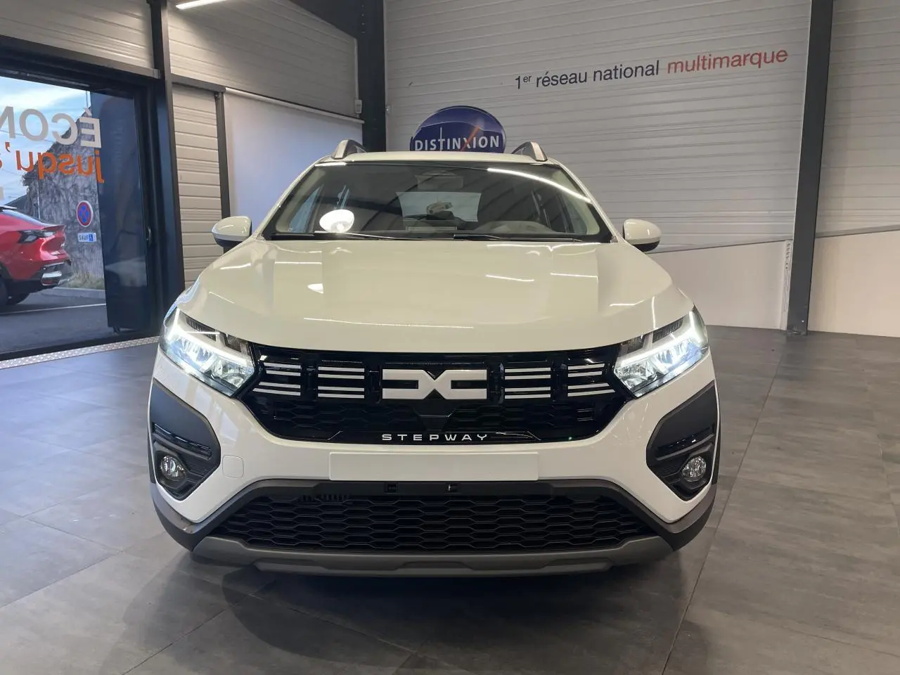 Vue de face d'une Dacia Sandero Stepway blanche Glacier avec calandre noire et signature lumineuse LED allumée.