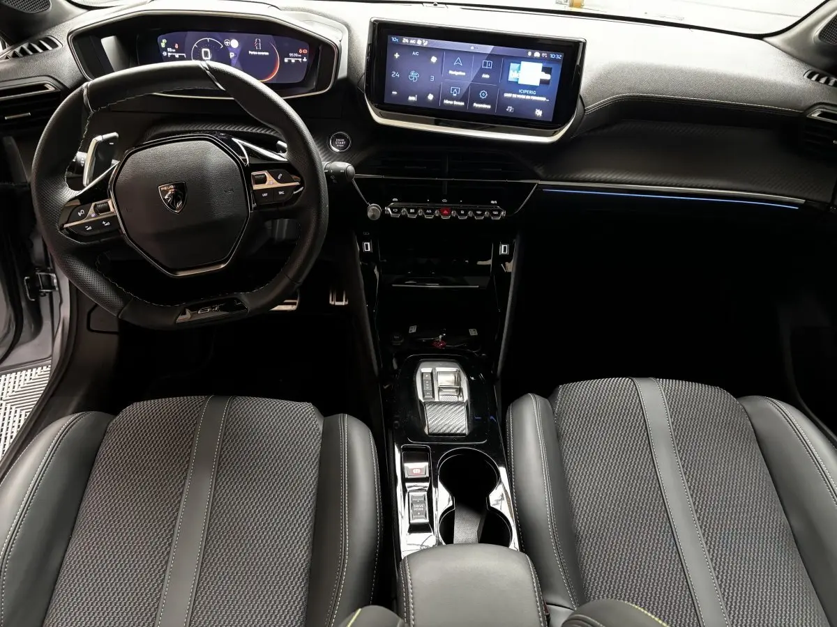 Intérieur de la Peugeot 208 Hybrid GT 2025, vue avant centrée sur le volant cuir alu et l’écran tactile central.