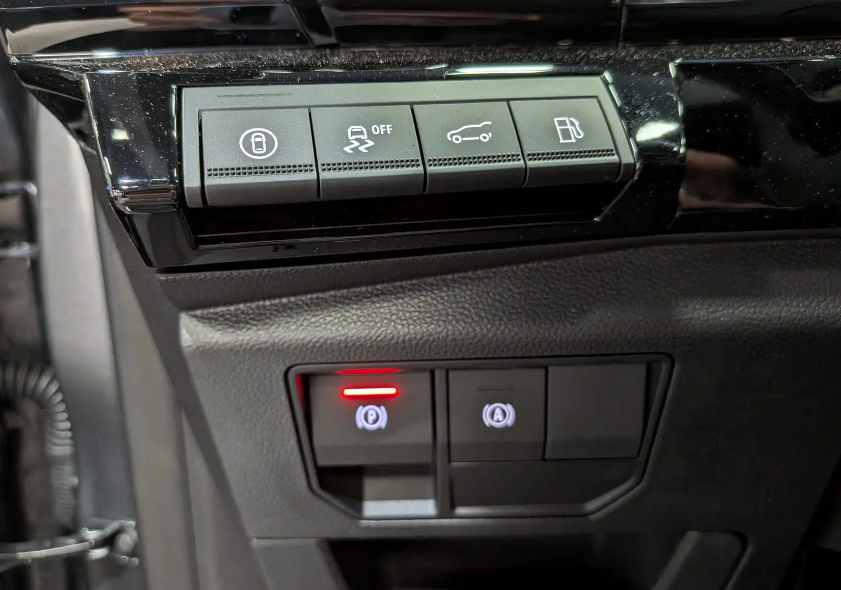 Gros plan sur les boutons de commande intérieurs noirs du Renault Rafale gris, avec témoin rouge actif au frein de parking.