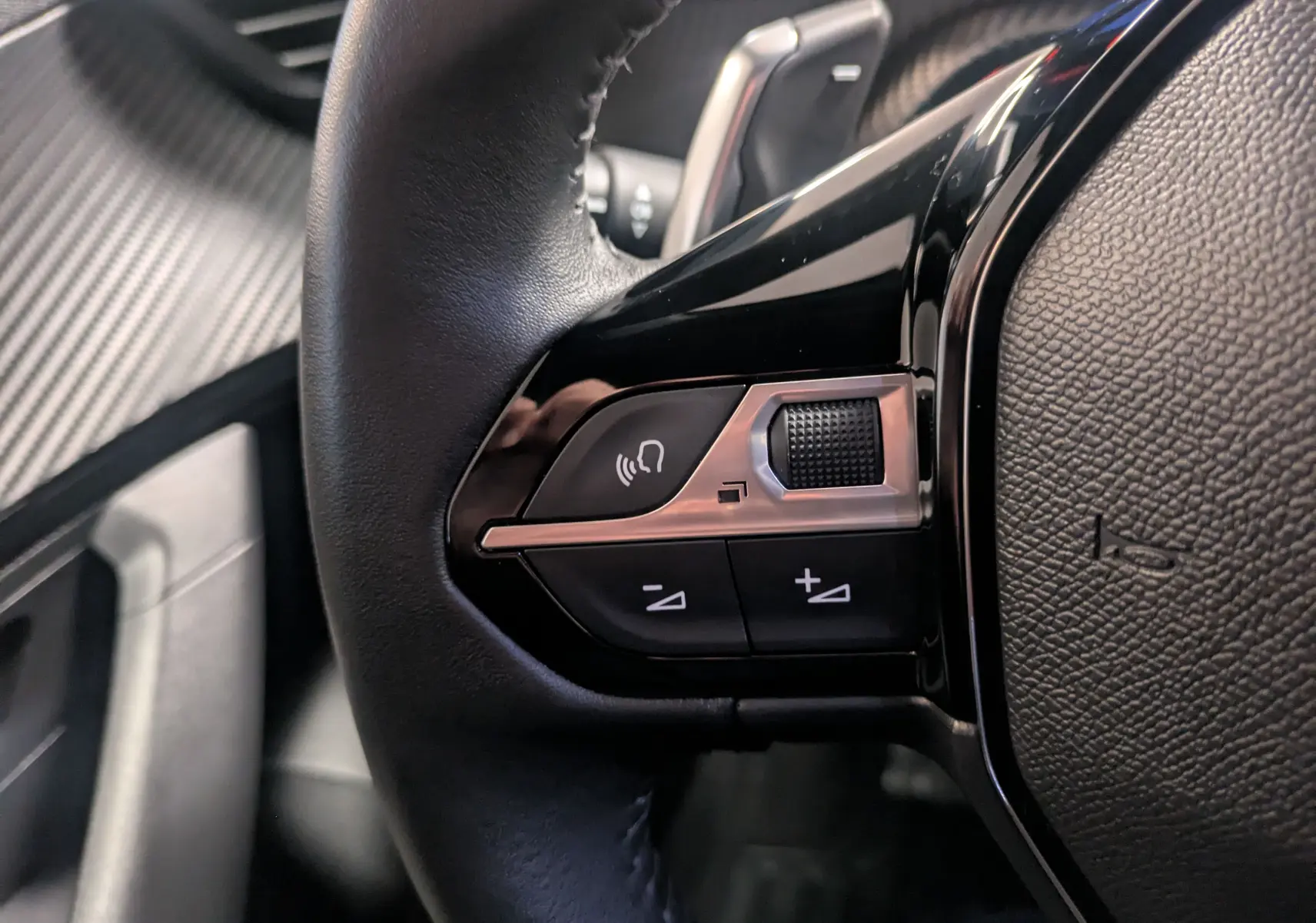 Gros plan sur les commandes gauche du volant noir du Peugeot 2008 2024 avec boutons de volume et appel mains libres.