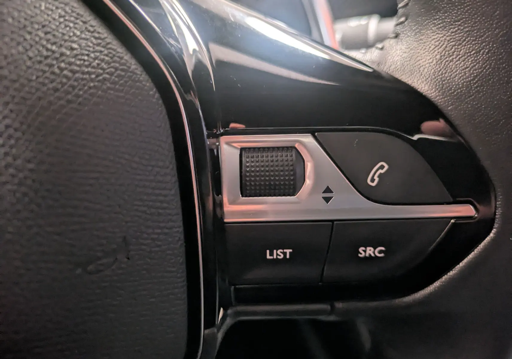 Gros plan sur les commandes du volant noir du Peugeot 2008 2024, boutons LIST, SRC et téléphone visibles.