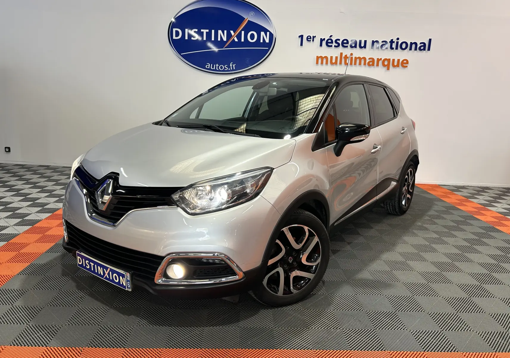 Renault Captur gris en 3/4 avant droit avec jantes alliage et feux allumés dans un showroom.