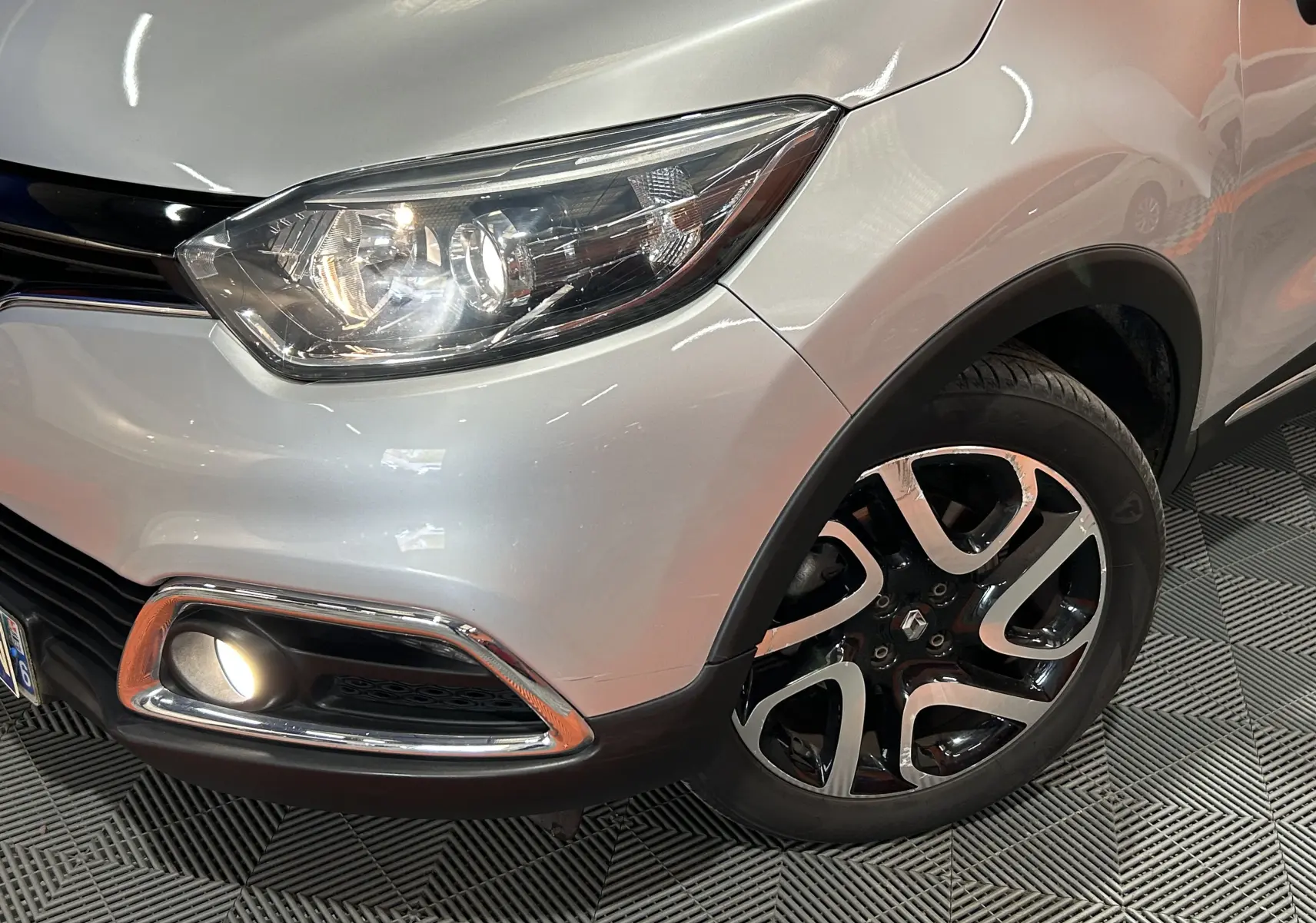 Gros plan sur l'avant droit gris du Renault Captur 2015 avec phare allumé et jante alliage distinctive.