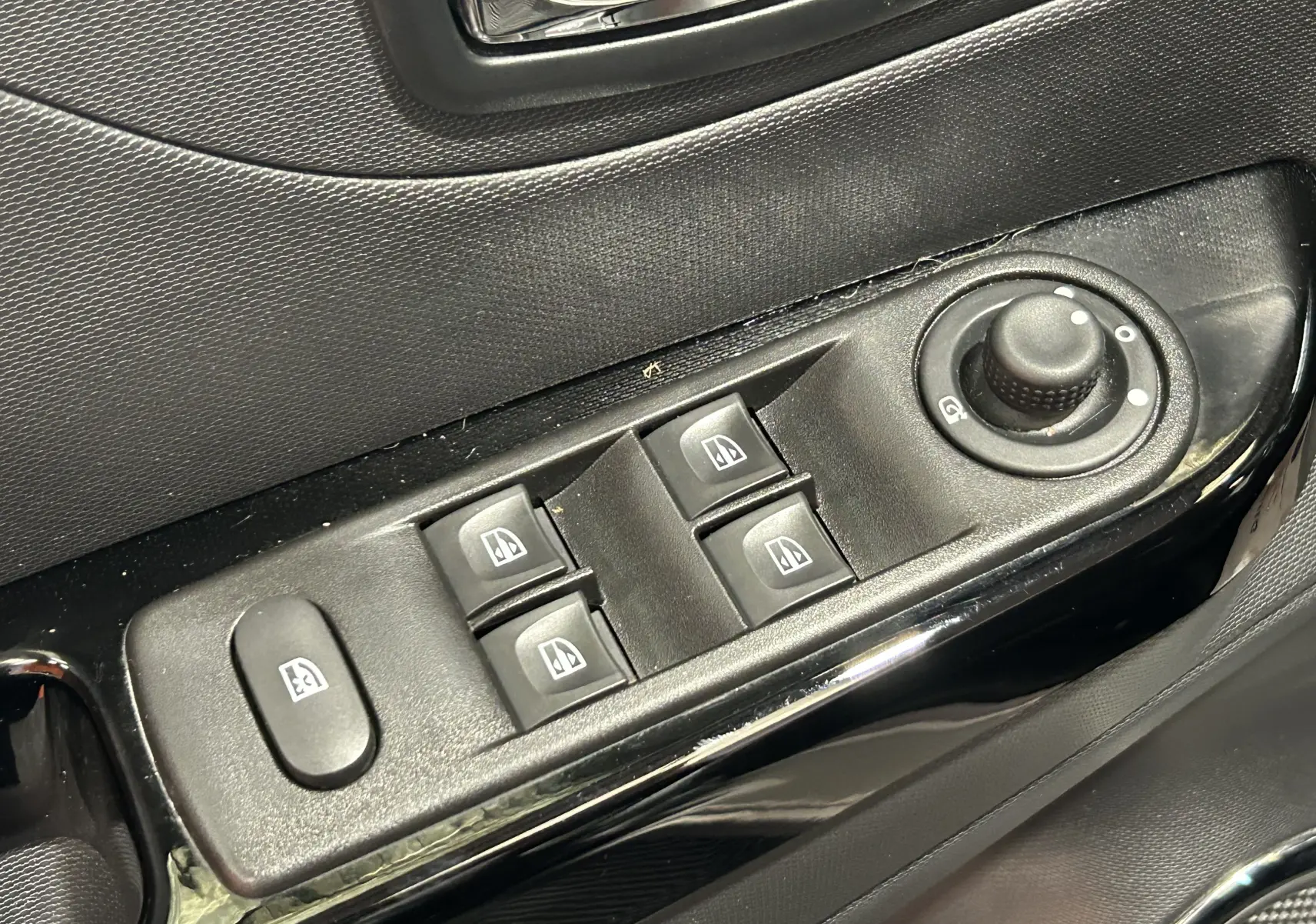 Gros plan sur les commandes de lève-vitres et réglage des rétroviseurs côté conducteur d’un Renault Captur gris.