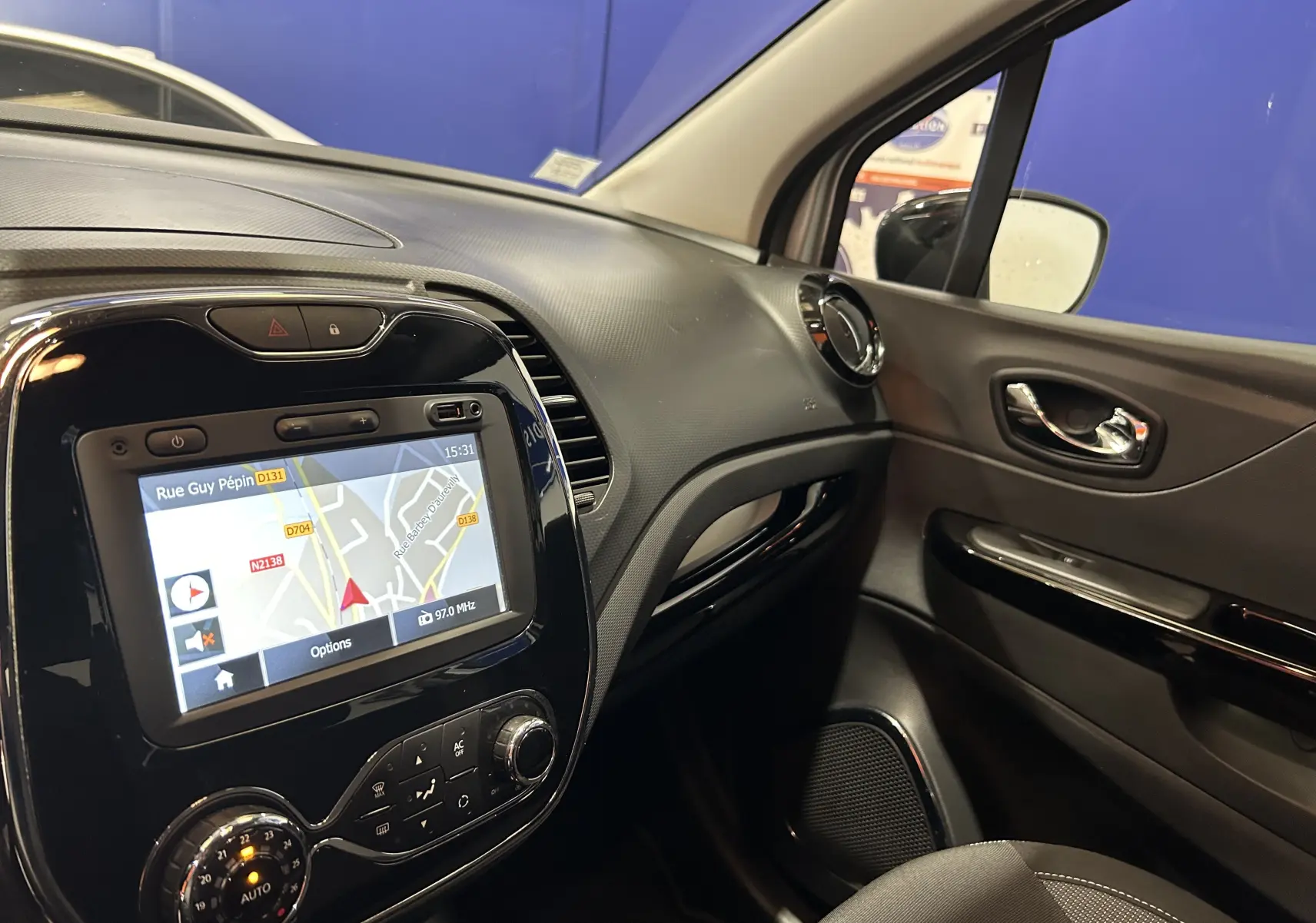Vue intérieure côté passager du tableau de bord du Renault Captur gris avec écran GPS allumé et commandes de climatisation.