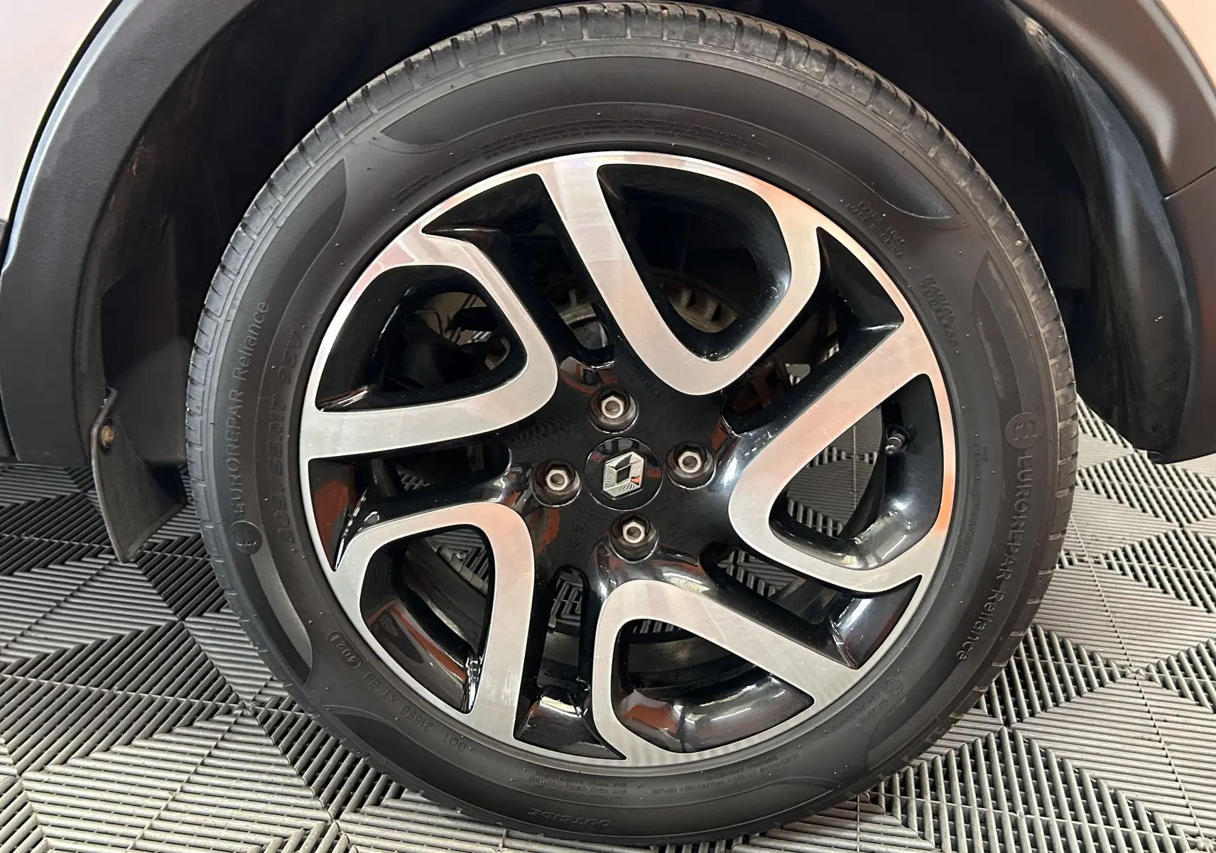 Gros plan sur la jante alliage bicolore noire et argent du Renault Captur gris, avec logo Renault au centre.