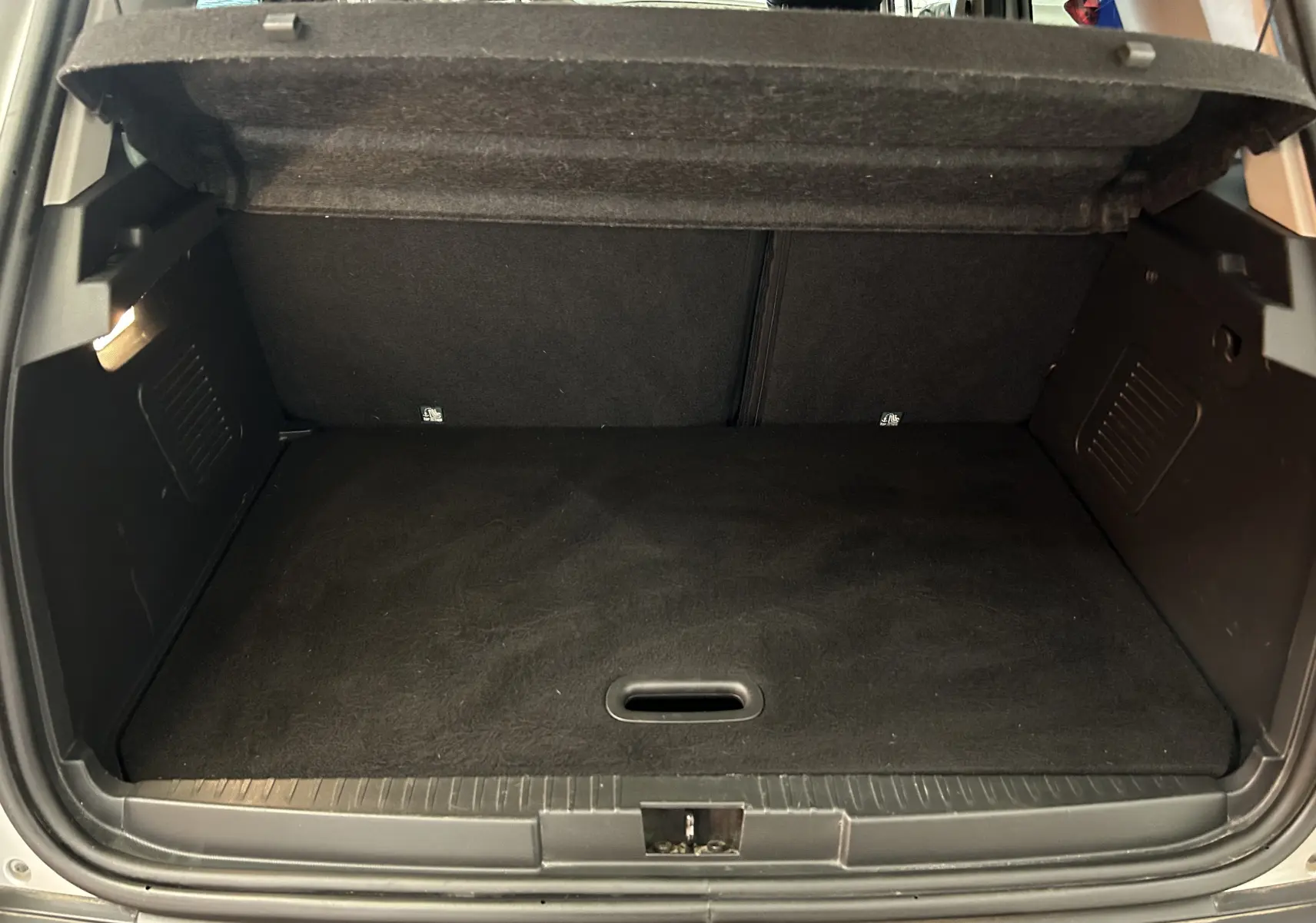 Coffre ouvert d'un Renault Captur gris 2015, vue arrière montrant l'espace de chargement vide et la moquette noire.