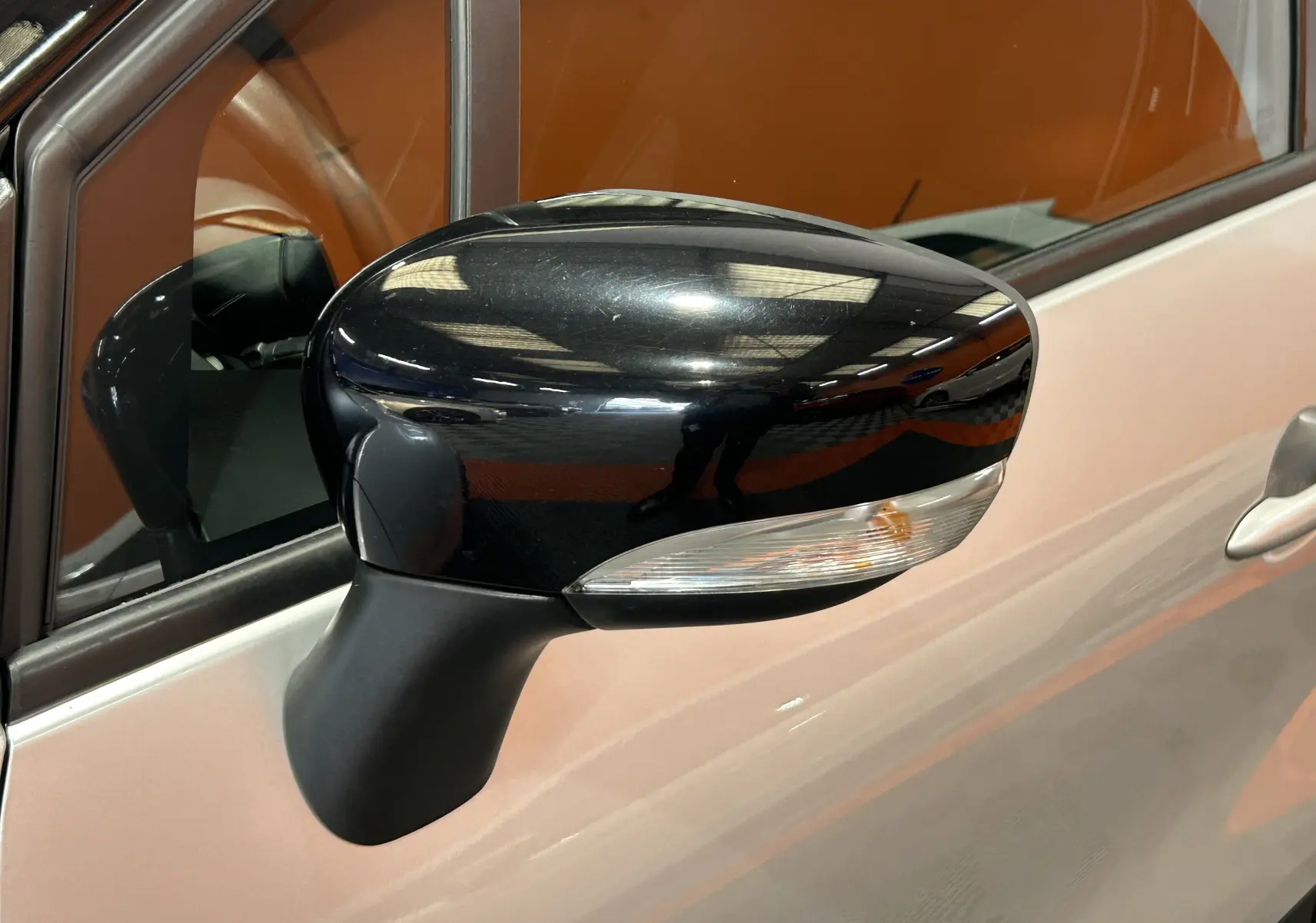 Rétroviseur noir en gros plan côté gauche d'un Renault Captur gris 2015 avec clignotant intégré.