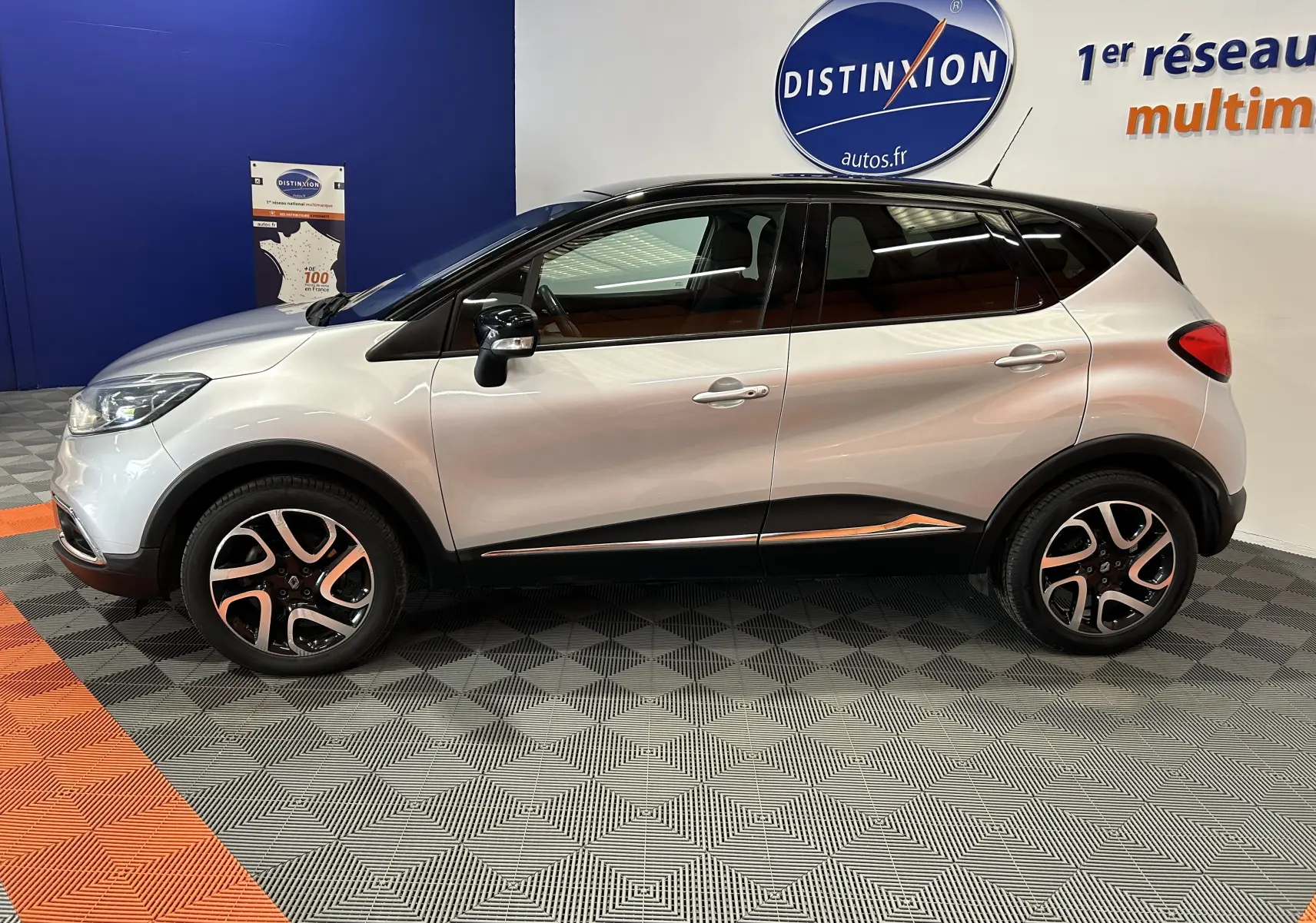 Profil côté gauche d'un Renault Captur gris 2015 avec toit noir, jantes alliage et détails chromés en intérieur showroom.