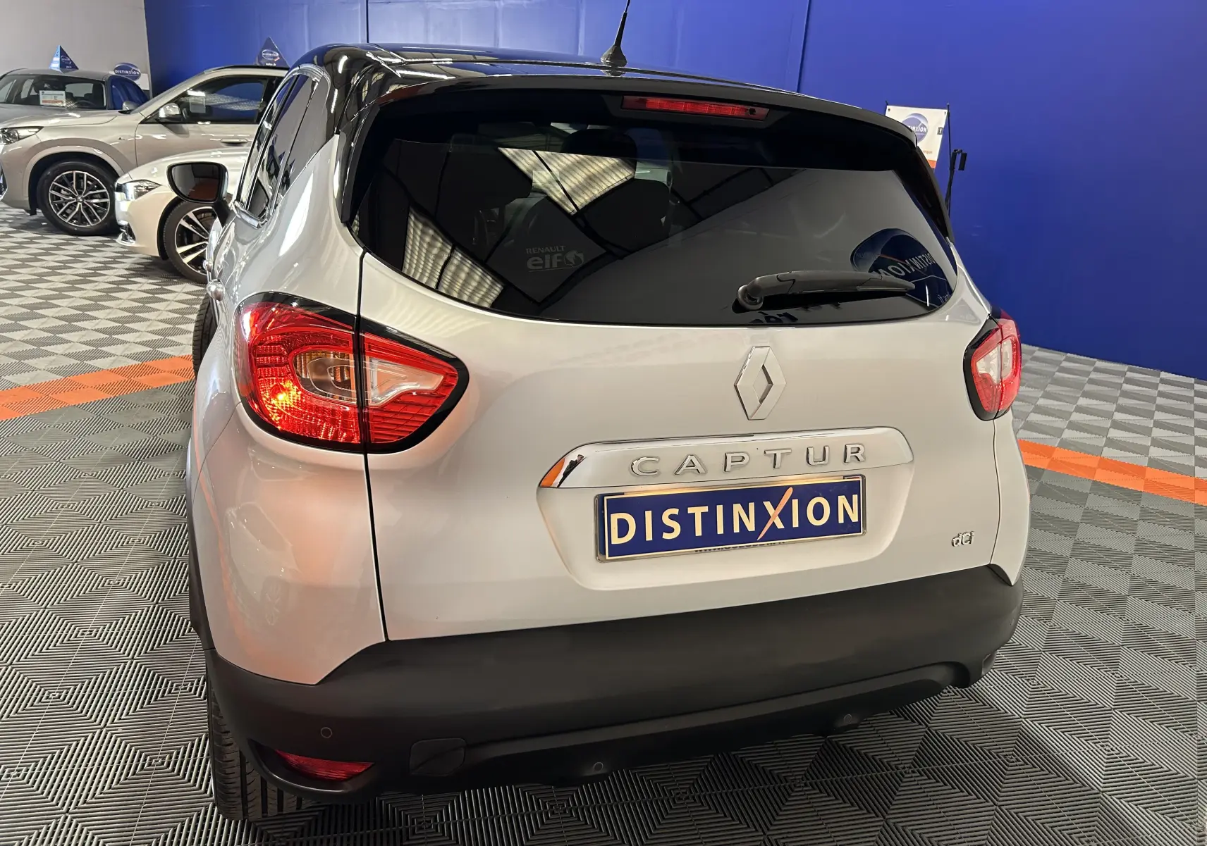 Vue arrière d'un Renault Captur gris 2015 avec feux allumés et plaque Distinxion dans un showroom.