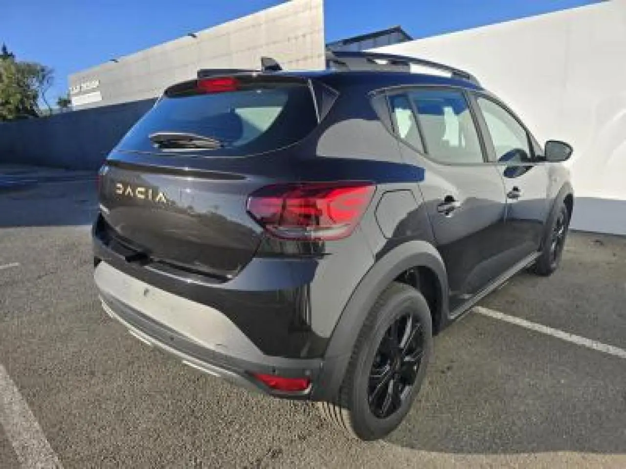 Vue 3/4 arrière droite d'une Dacia Sandero Stepway 2025 noir nacré avec jantes noires et barres de toit.