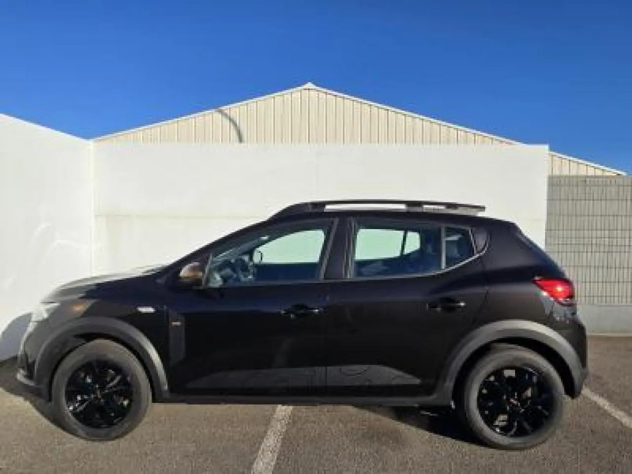 Profil côté gauche de la Dacia Sandero III Stepway noir nacré avec barres de toit et jantes noires en aluminium.