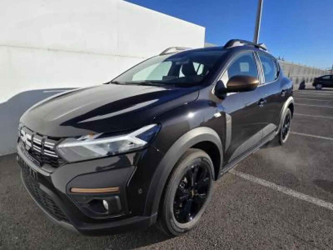 Dacia Sandero III Stepway noir nacré en 3/4 avant droit avec barres de toit brun cuirvré et jantes noires.