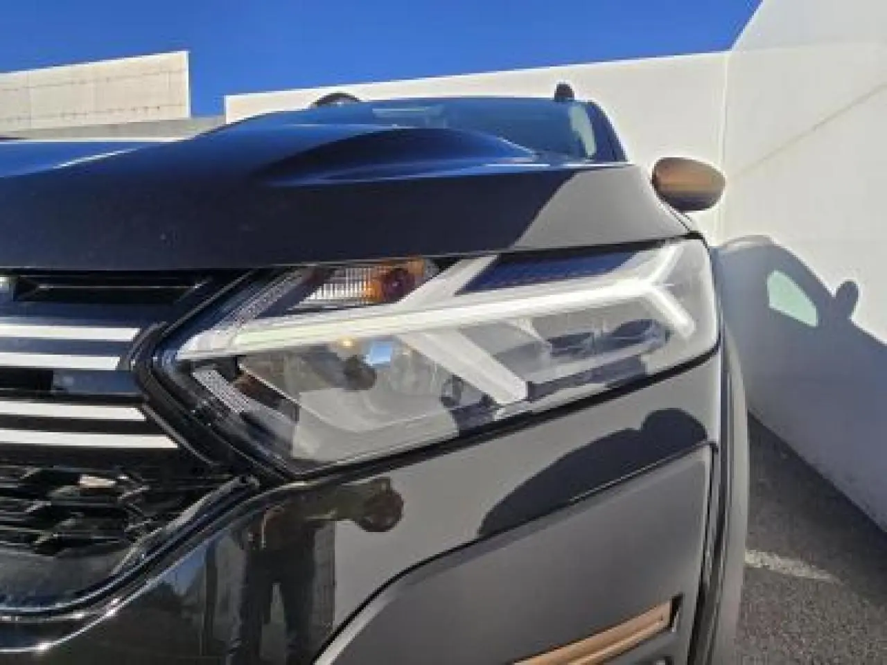 Gros plan sur le phare avant droit et la calandre noire nacrée du Dacia Sandero III Stepway avec détails chromés.