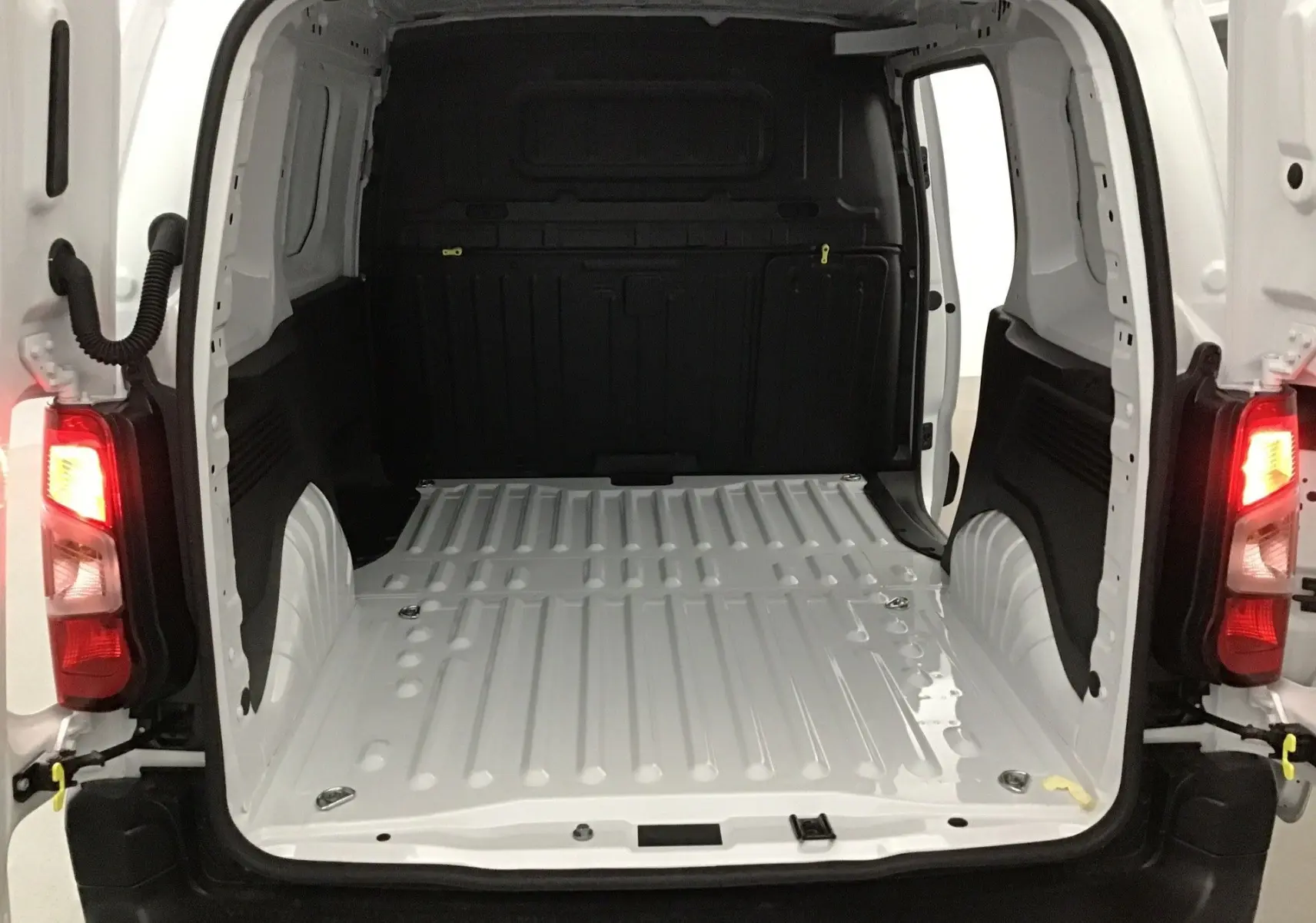 Vue arrière du Peugeot Partner blanc 2025, montrant l’espace de chargement vide avec portes ouvertes et feux arrière allumés.