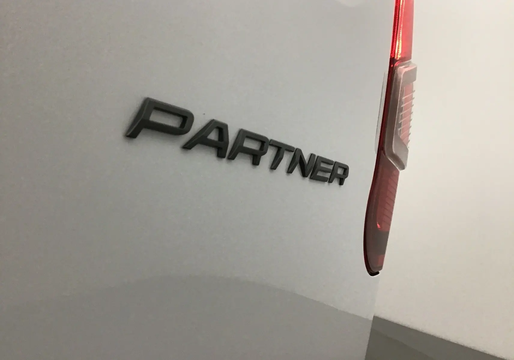 Gros plan sur l'arrière droit blanc du Peugeot Partner 2025, mettant en valeur le logo "PARTNER" et le feu arrière vertical.