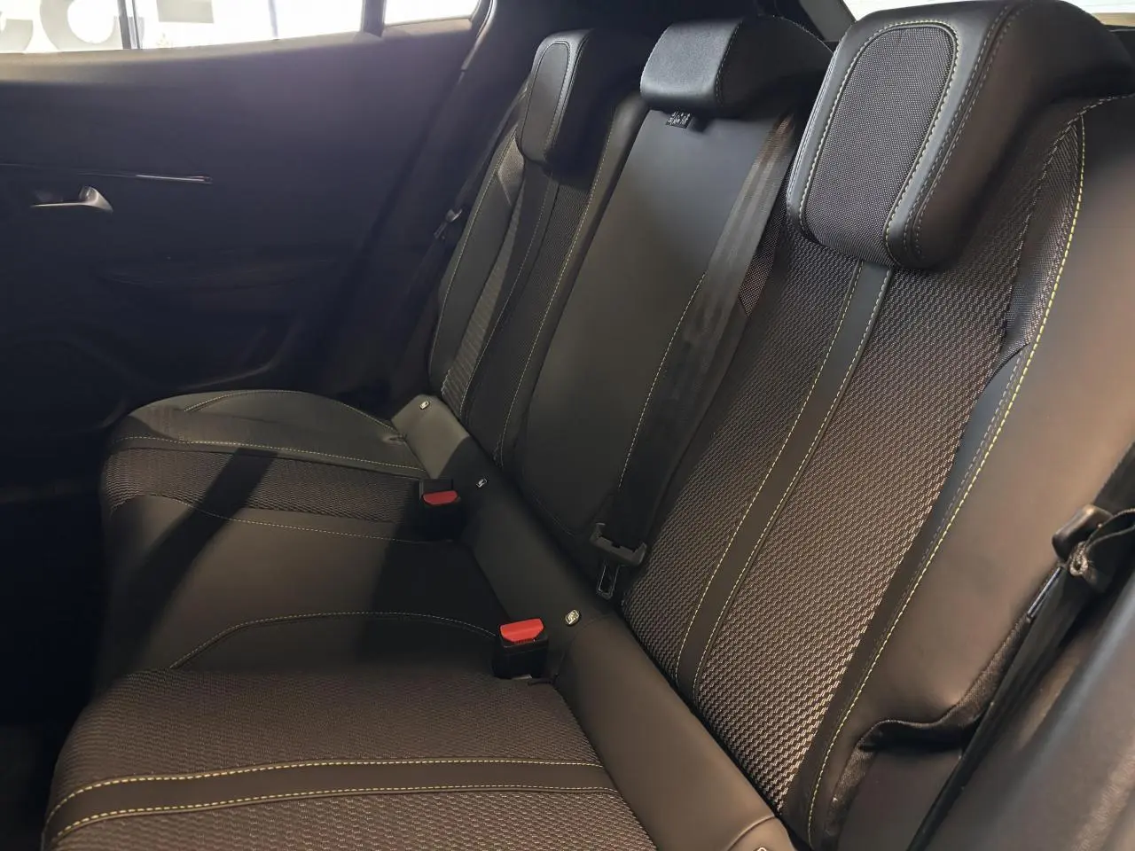 Vue rapprochée des sièges arrière noirs avec surpiqûres vertes du Peugeot 2008 hybride 2025.