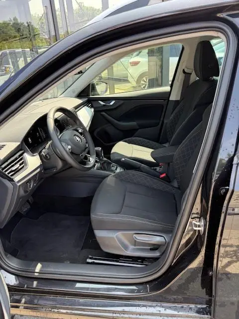 Vue intérieure côté conducteur du Skoda Kamiq noir 2024, montrant sièges tissu noir et tableau de bord moderne avec écran tactile.