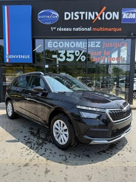 Vue 3/4 avant gauche d'un Skoda Kamiq noir 2024 garé devant une concession Distinxion avec reflets sur la carrosserie.