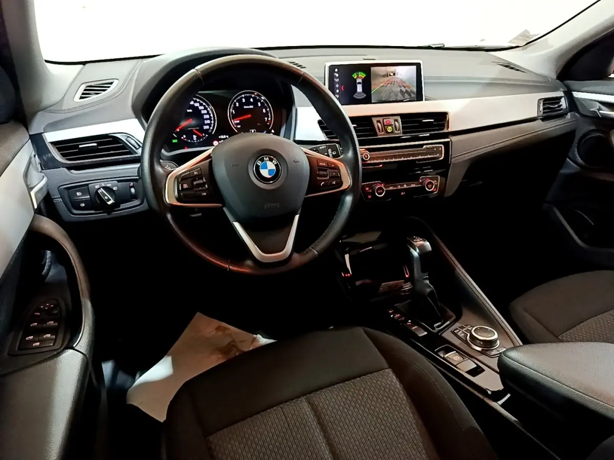 Vue intérieure avant du tableau de bord et volant cuir noir de la BMW X2 xDrive25e avec écran tactile et commandes multifonctions.