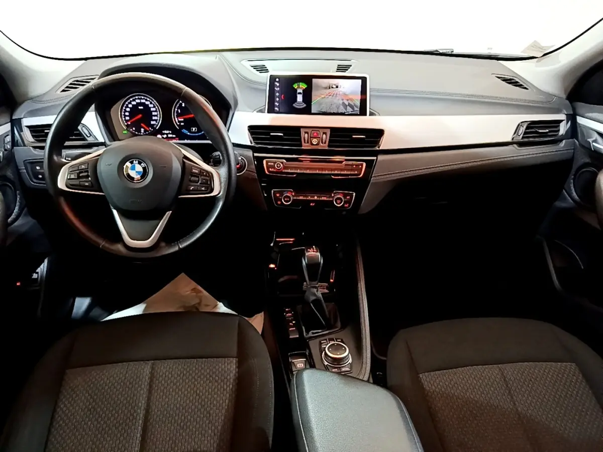 Vue intérieure avant du tableau de bord et volant noir de la BMW X2 xDrive25e avec écran tactile central allumé.