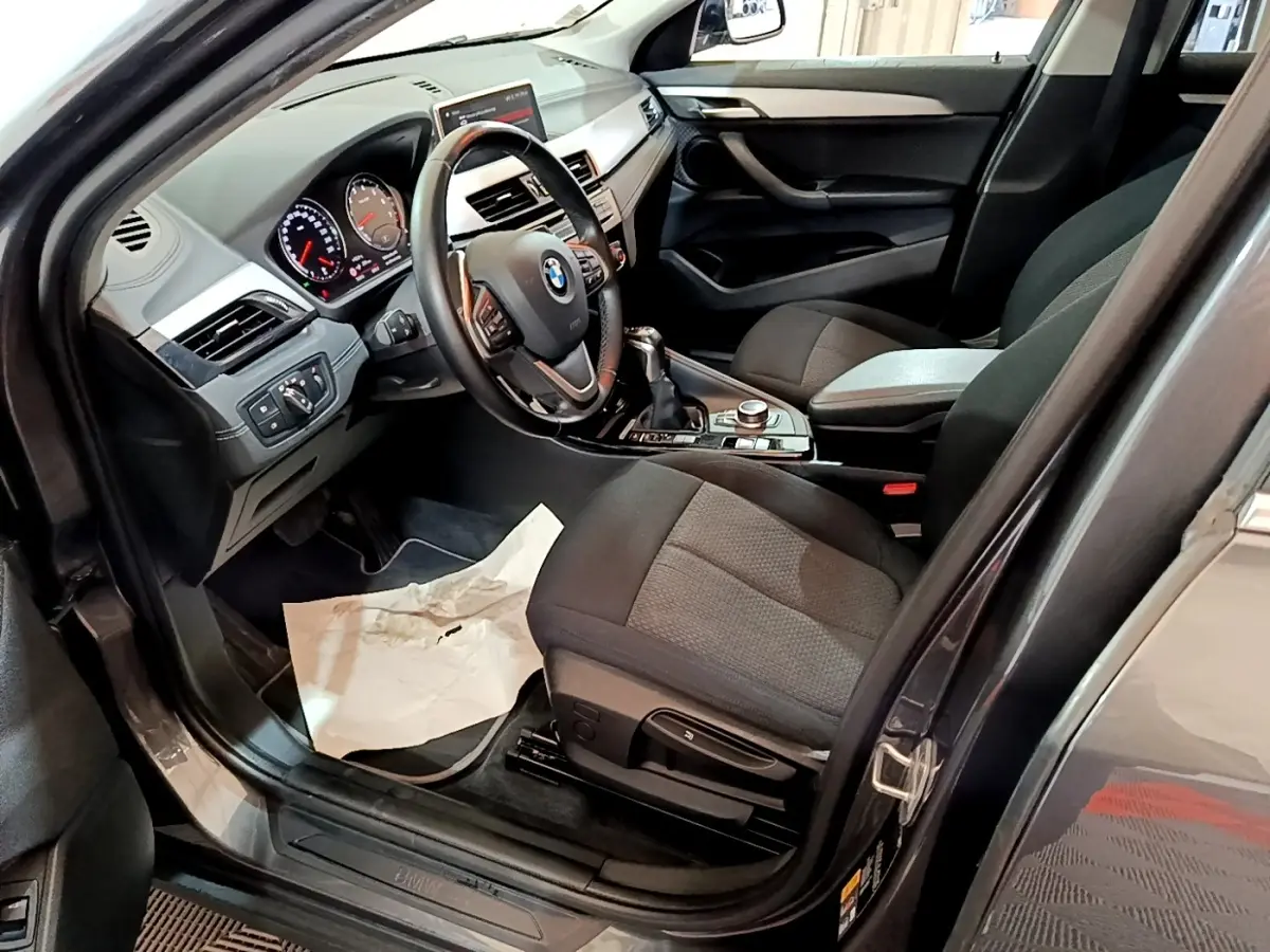 Vue intérieure côté conducteur de la BMW X2 xDrive25e noire, avec tableau de bord et volant multifonctions en cuir.