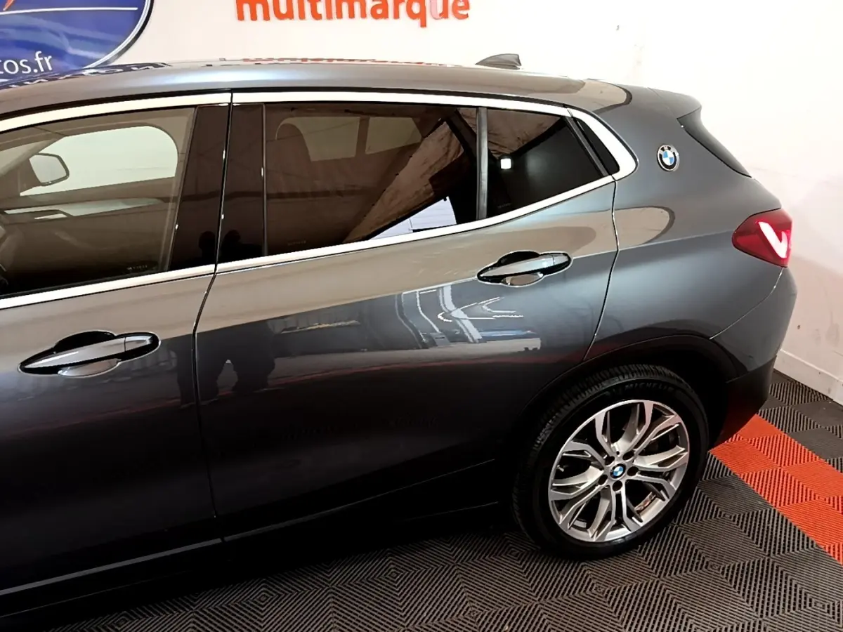 Vue latérale droite sur l'arrière d'un BMW X2 hybride rechargeable gris foncé avec jantes alliage et logo BMW sur l'aile arrière.