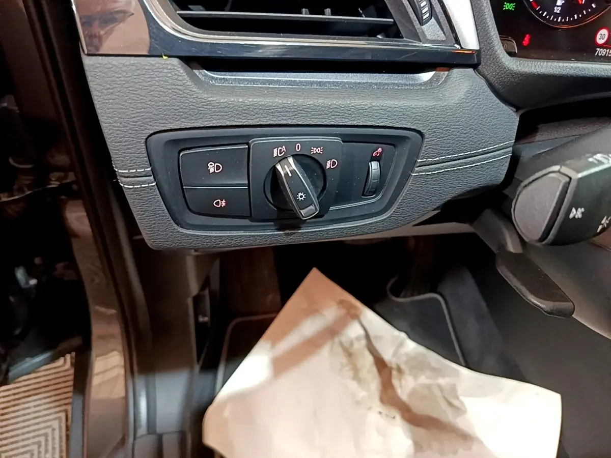 Gros plan sur le panneau de commande des phares à gauche du volant dans l'habitacle noir de la BMW X2 hybride.