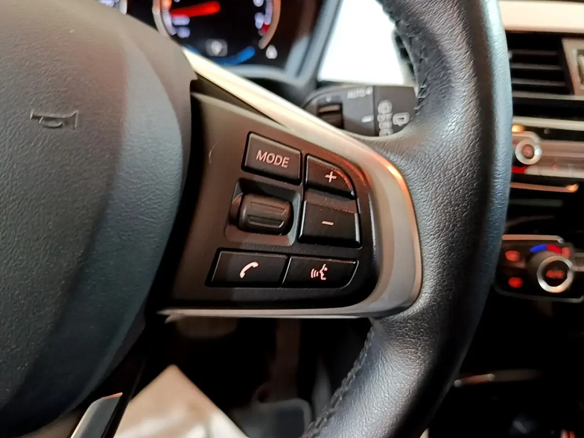 Gros plan sur le côté gauche du volant cuir noir de la BMW X2 xDrive25e avec commandes multimédia intégrées.