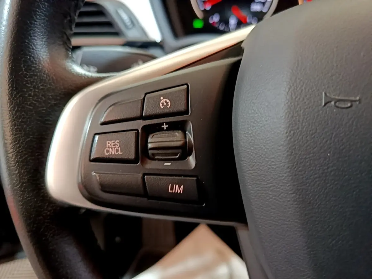 Gros plan sur les commandes noires du régulateur de vitesse au volant cuir noir de la BMW X2 hybride rechargeable.