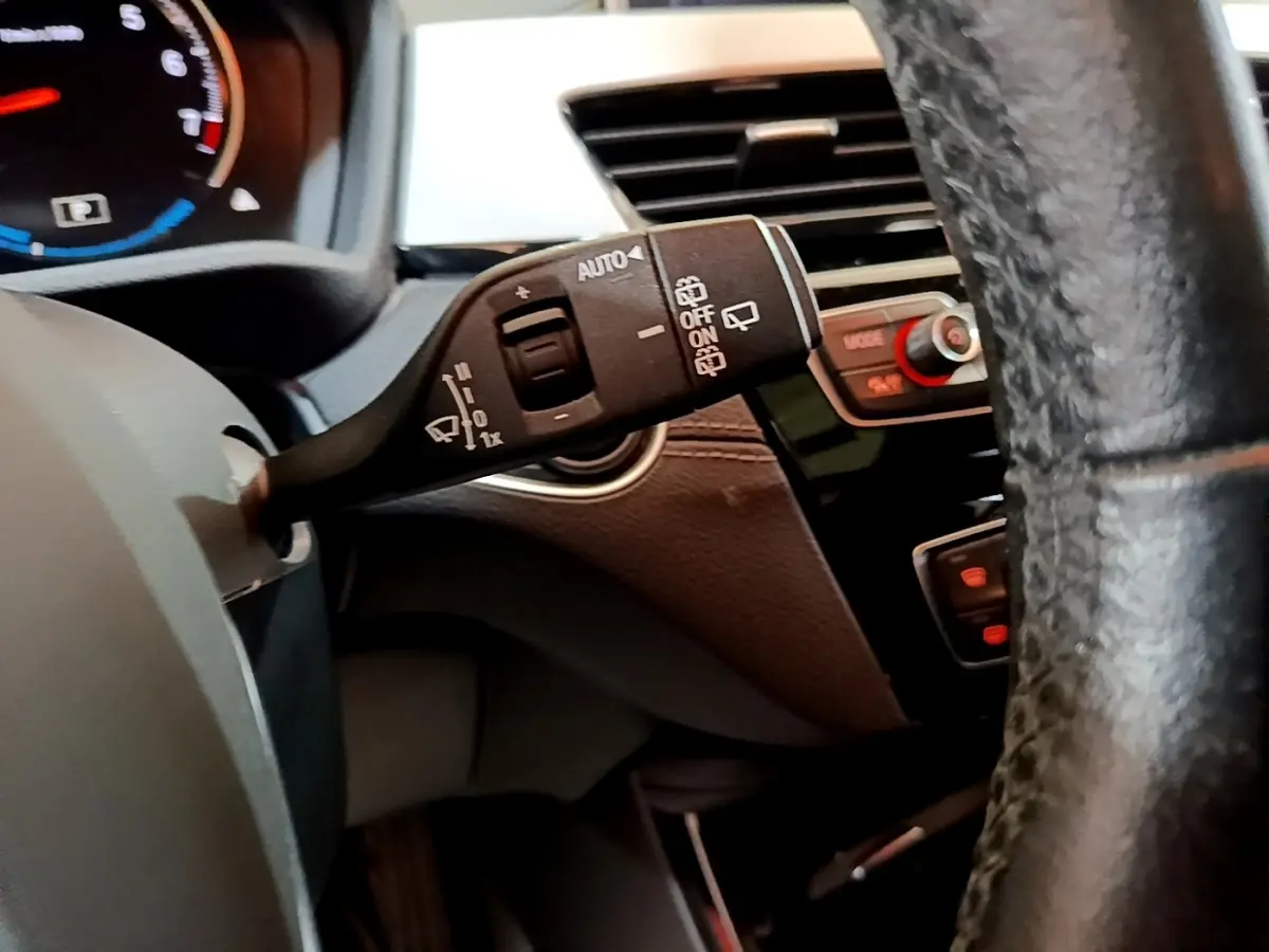 Gros plan sur la manette d’essuie-glace à gauche du volant cuir noir dans l’habitacle sombre d’une BMW X2 hybride rechargeable.