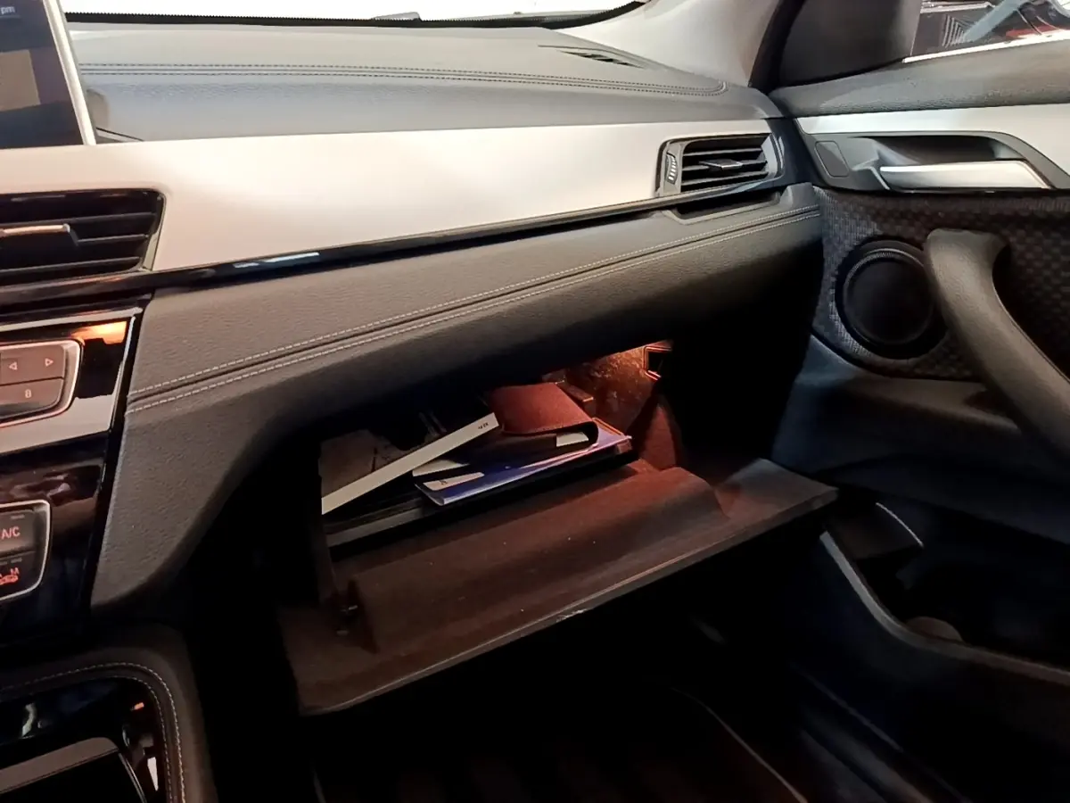 Vue intérieure côté passager du BMW X2 xDrive25e 2020 avec boîte à gants ouverte et éclairage intérieur orange.