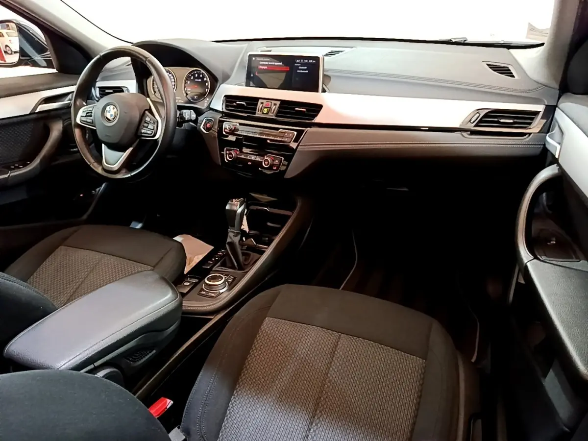Intérieur BMW X2 xDrive25e 2020 vu de l'avant droit, tableau de bord noir avec écran tactile central et volant multifonctions.
