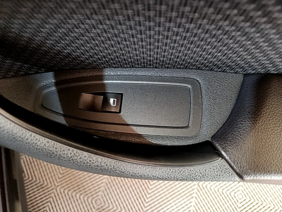 Gros plan sur le bouton de commande de lève-vitre intérieur en plastique noir, sur la porte côté conducteur d’un BMW X2 hybride.