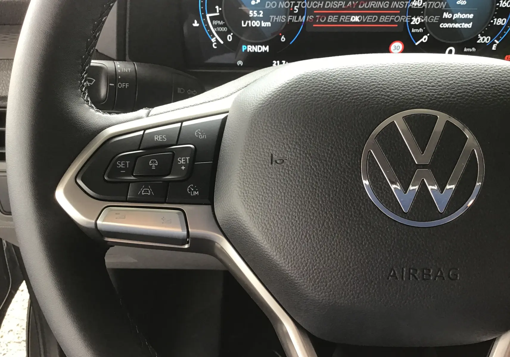 Gros plan sur le volant multifonction du Volkswagen Transporter T7 gris Stone, avec tableau de bord numérique en arrière-plan.