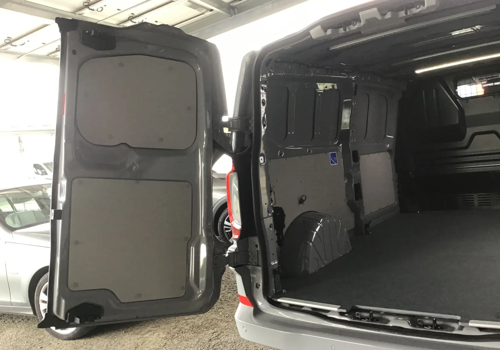 Vue arrière ouverte du Volkswagen Transporter T7 gris stone montrant l'espace de chargement vide et les portes battantes.