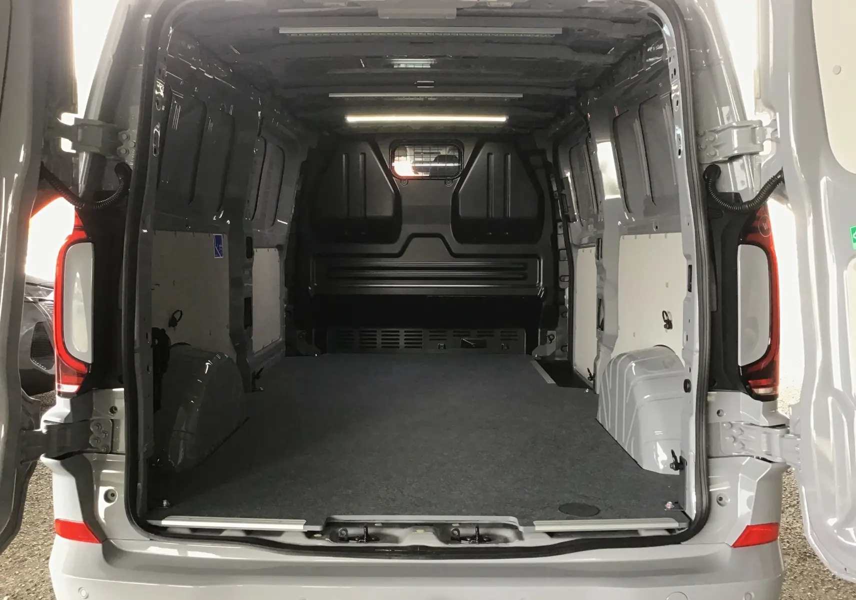 Vue arrière ouverte du Volkswagen Transporter T7 gris stone montrant l'espace de chargement vide et l'aménagement intérieur utilitaire.