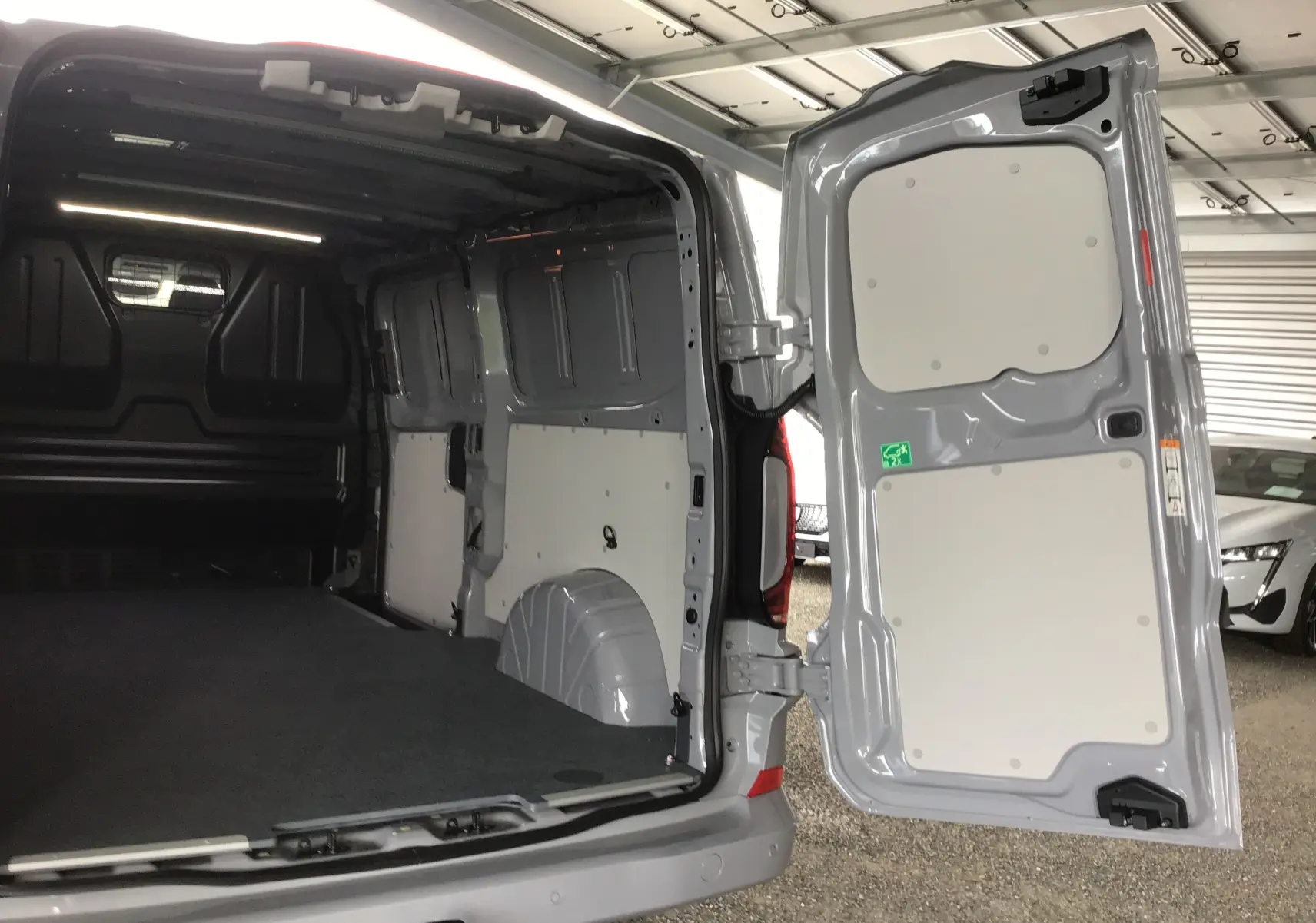 Vue arrière ouverte du Volkswagen Transporter T7 gris stone, montrant l'espace de chargement vide et les portes battantes.