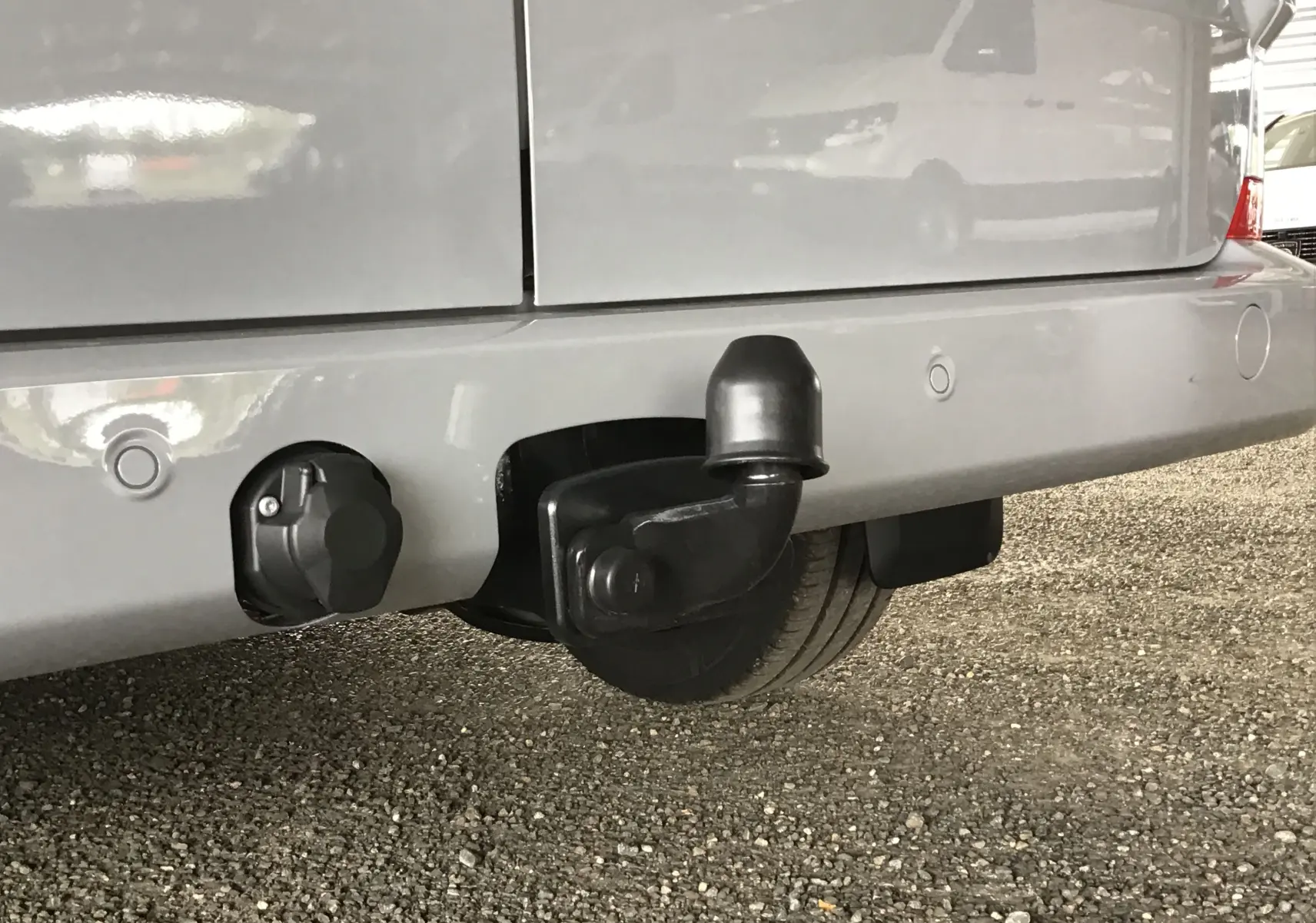 Gros plan sur l'attelage d'un Volkswagen Transporter T7 gris stone, vue arrière basse avec prise électrique visible.