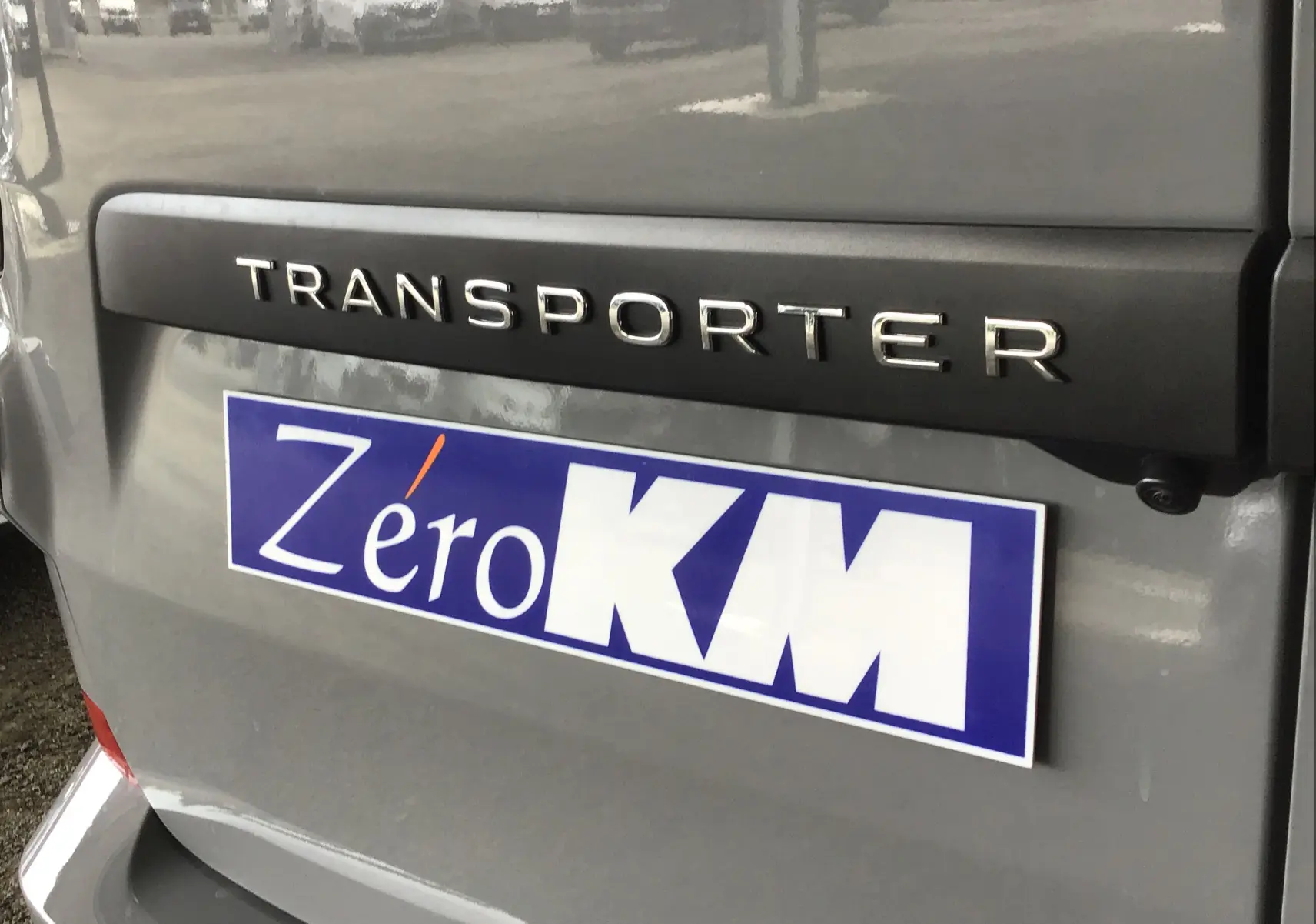 Gros plan sur l'arrière gris stone du Volkswagen Transporter T7 avec logo et plaque Zéro KM visible.