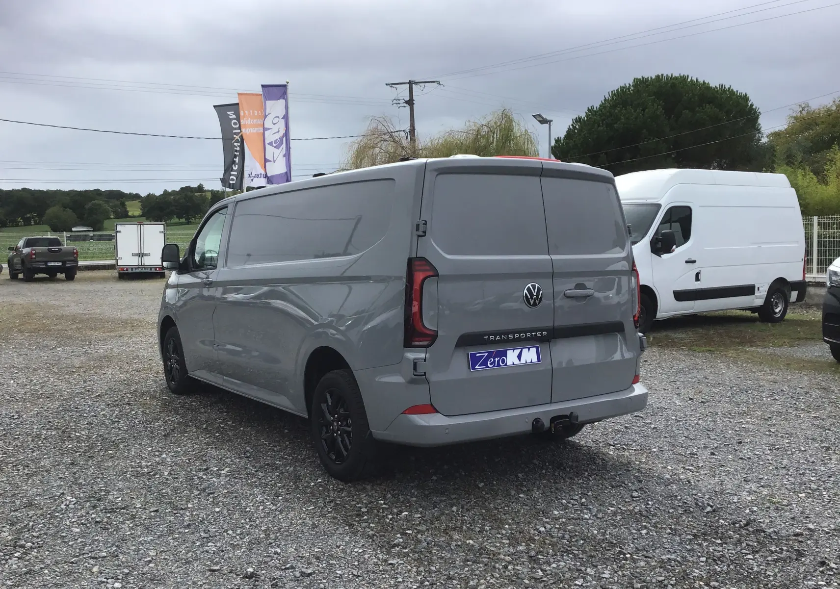 Vue 3/4 arrière droite d'un Volkswagen Transporter T7 gris stone avec barres de toit repliables et jantes noires.