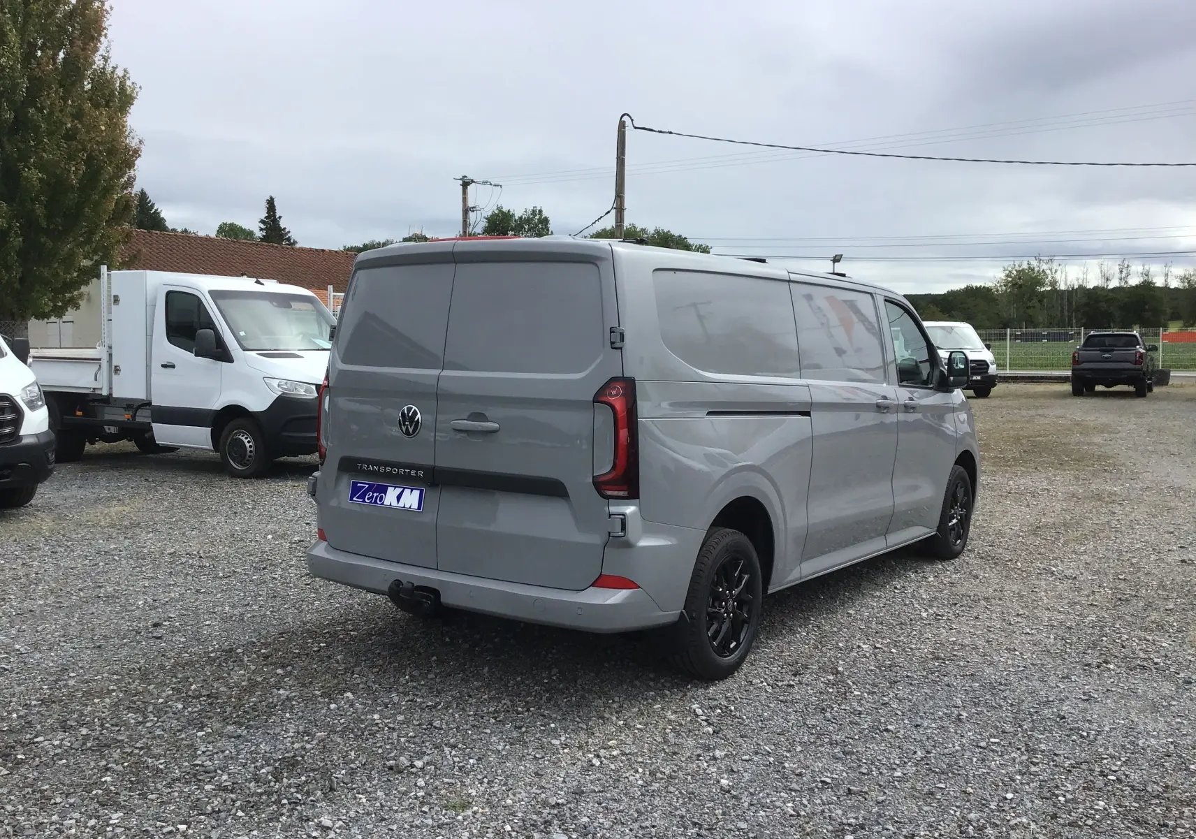 Volkswagen Transporter gris Stone vu en 3/4 arrière droit, avec barres de toit repliables et jantes noires.