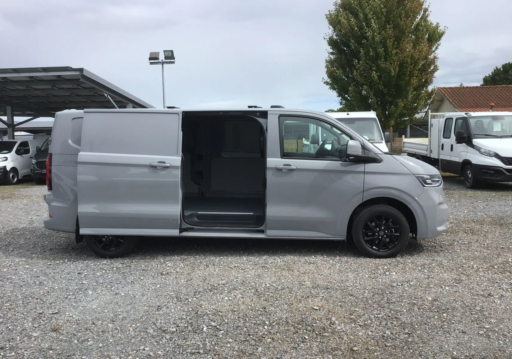 Vue latérale droite du Volkswagen Transporter T7 gris Stone avec porte coulissante ouverte et jantes noires.
