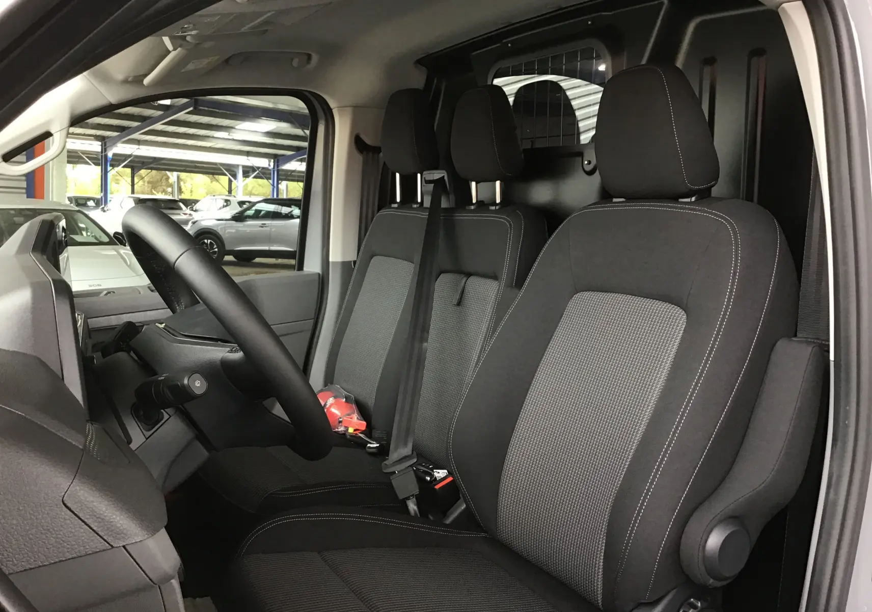 Vue intérieure côté conducteur du Volkswagen Transporter T7 gris Stone, montrant les sièges avant en tissu noir et gris.