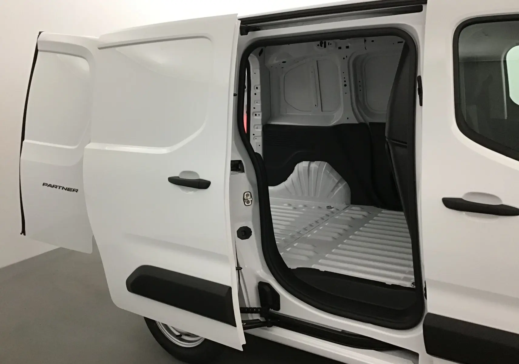 Vue latérale droite d'un Peugeot Partner blanc avec porte coulissante ouverte dévoilant l'espace de chargement vide.