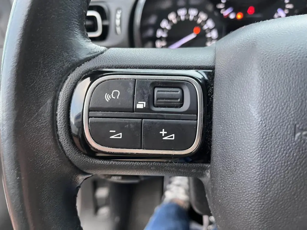 Gros plan sur les commandes audio au volant d'une Citroën C3 2019, finition Origins, volant en cuir noir.