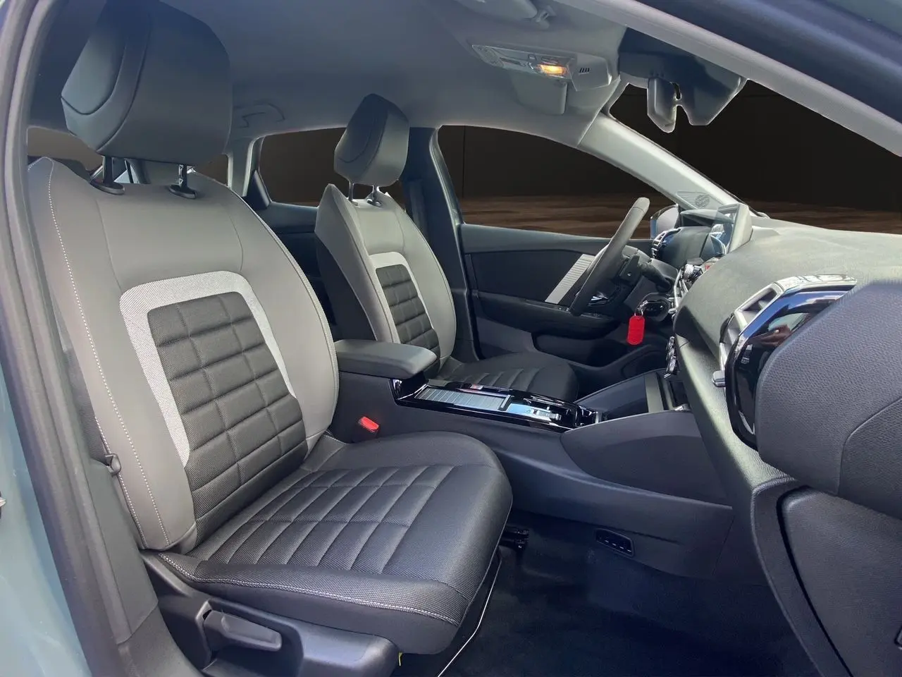 Intérieur avant de la Citroën C4 hybride 2025, sièges tissu gris noir avec console centrale et tableau de bord visibles.
