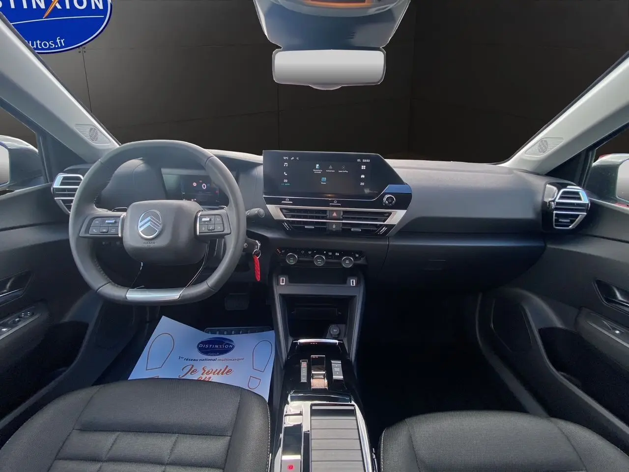 Intérieur de la Citroën C4 2025 vue de face, tableau de bord noir avec écran tactile central et volant multifonctions.