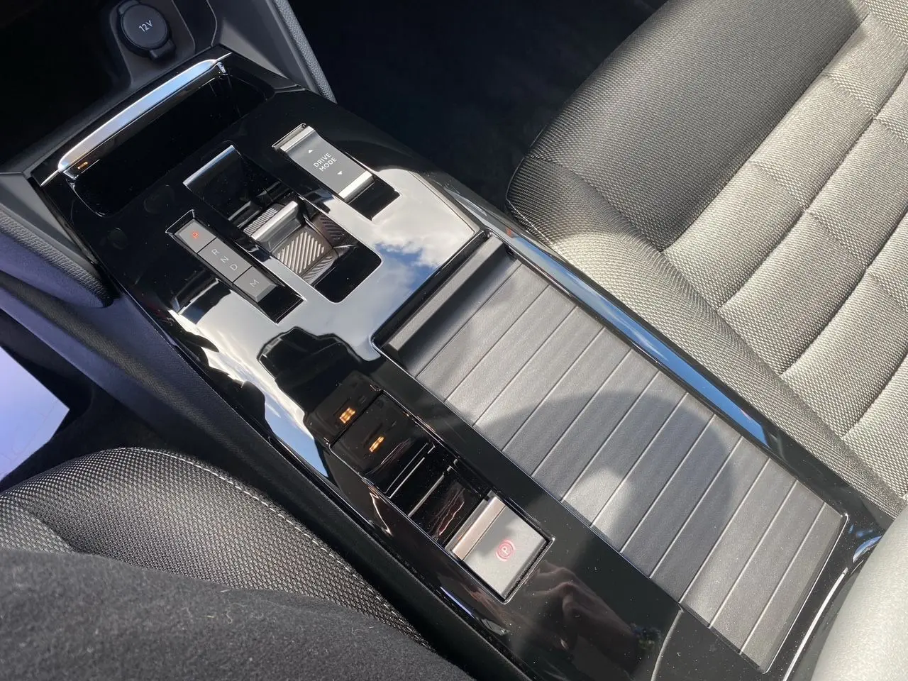 Gros plan sur la console centrale noire brillante et le siège tissu gris foncé de la Citroën C4 hybride 2025.