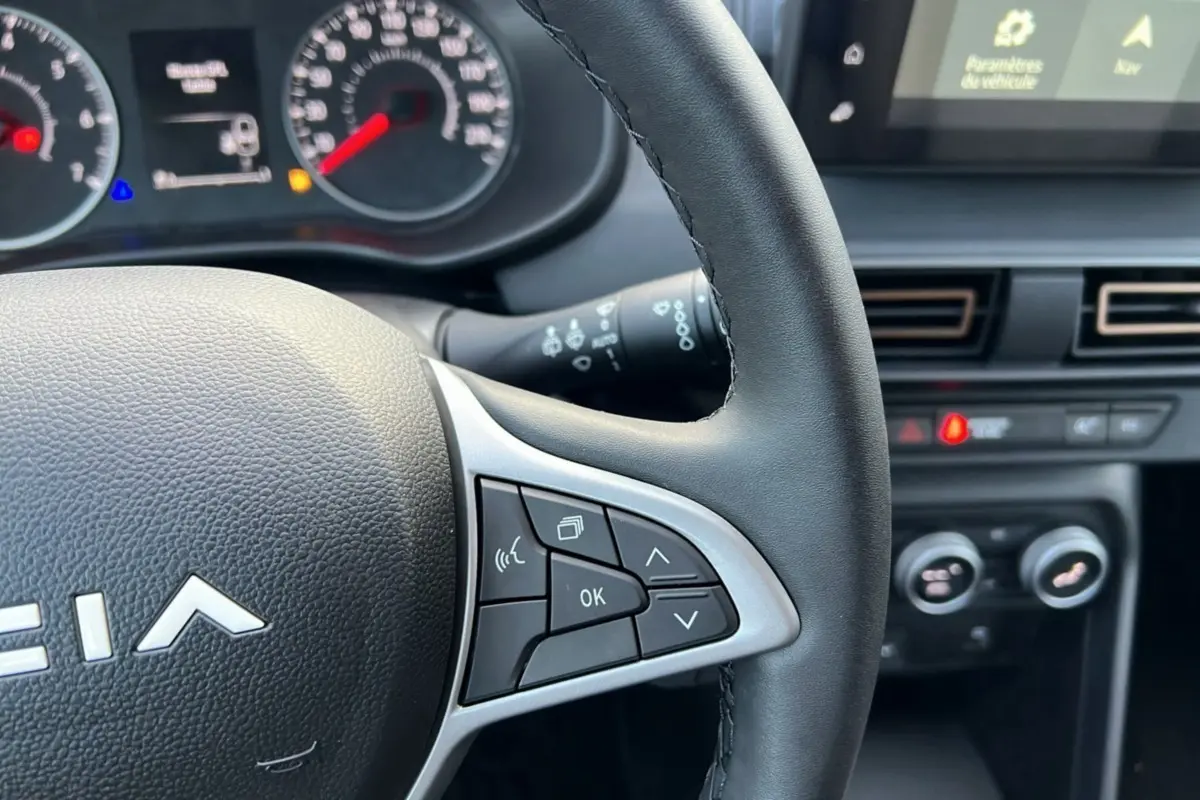 Gros plan sur le volant noir de la Dacia Sandero Stepway 2024, avec commandes multifonctions et tableau de bord en arrière-plan.